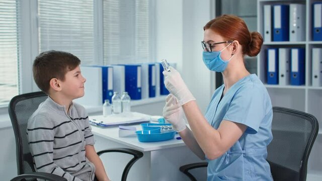 vaccination, doctor in protective gloves and glasses typing vaccine with syringe then injects the boy patient at hospital office during quarantine