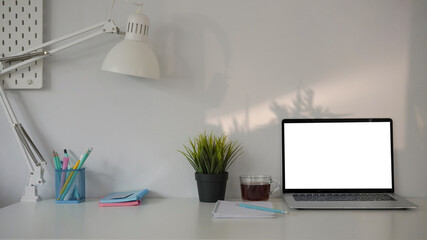 Home office desk with computer laptop, coffee cup, notebook, plant and pencil holder.