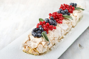Meringue dessert Pavlova cake with fresh berries on top on a light wooden background.