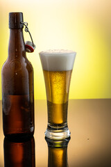 pouring beer into beer glass from bottle on yellow background