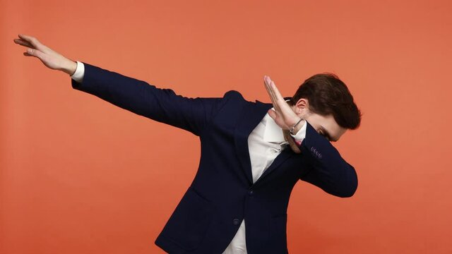 Positive young office worker showing dab dance pose, triumph gesture, expressing happiness and happiness, celebrating success, dabbing trends. Indoor studio shot isolated on orange background
