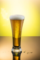 tall transparent glass on yellow background with beer and foam on the surface