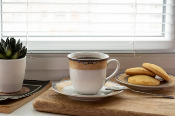 Cup of coffee, lemon vanilla cookies on a wooden board, decorative flower, book on the background of a window on a rainy day
