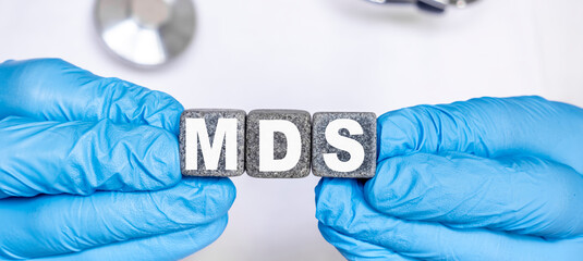MDS Myelo dysplastic syndrome - word from stone blocks with letters holding by a doctor's hands in medical protective gloves