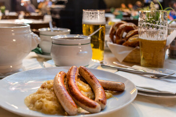 Classic German dinner of fried sausages with braised cabbage on large white plates with light beer, standing on table in restaurant interior.