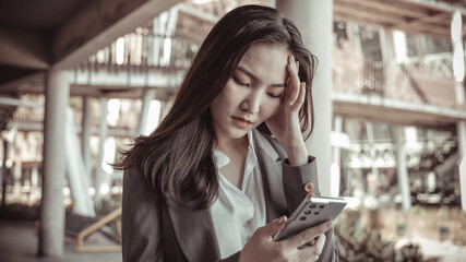 Fototapeta premium Young woman in a gray suit looks tense over working on a smartphone, Young business woman is stressed by work because the data sent from the smartphone is wrong, Anxious, Sad, Wrong, Depressed.