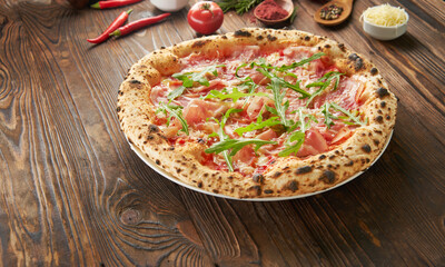 Original italian neapolitan pizza with parma ham and fresh arugula on wooden background with ingredients. Fast food eating concept