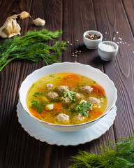 Soup with meatballs in a white plate with sauce and herbs on a wooden table. Photo for the menu of a restaurant, cafe, canteen. 