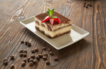 Traditional italian tiramisu dessert on white plate, wooden background with coffee beans