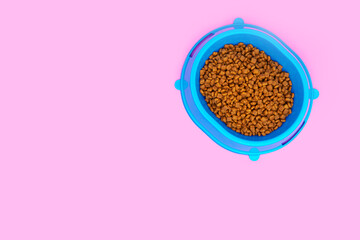 Full blue bowl of cat food on a pink background.