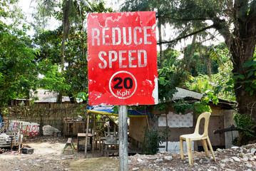 Bright red colored Reduce Speed road signage standing in front of a poor depressed neighborhood on Boracay Island, Philippines, Asia