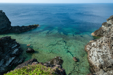 Impressive marine scene seen from a high cliff. Well designed coral platform with large rocks, transparent sea and a deep navy blue in the background.