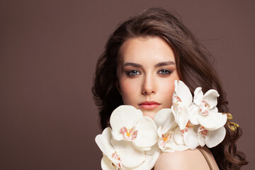 Young pretty woman face with healthy clear skin and white orchid flowers portrait. Facial treatment and skin care concept