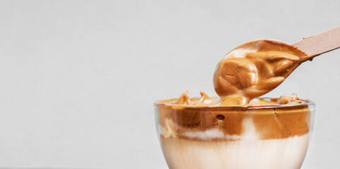 Fluffy coffee with milk and and spoon on gray background. Сream foam. Coffee drink. Glass сreamy caramel whipped latte