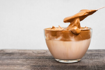 Glass cup  fluffy coffee with milk and spoon on a wooden table. Coffee drink. Creamy caramel whipped latte