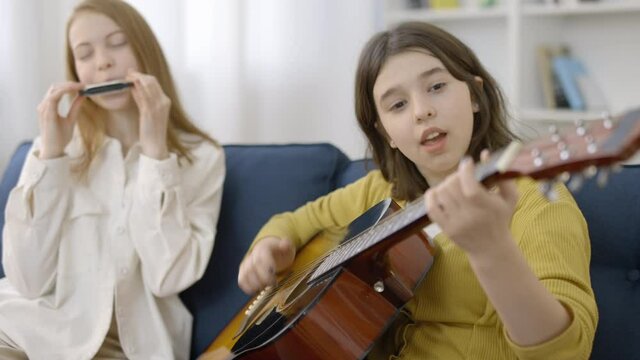 Teenage girls preparing for music concert, playing acoustic guitar and harmonica