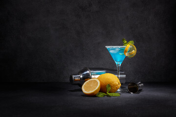 Blue cocktail. Glass with blue curacao cocktail, fresh mint and lemon, bar tools on dark grey background with copy space.