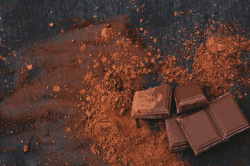 Cocoa powder and broken chocolate pieces on black background. Top view