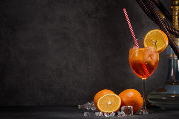Hookah (shisha), glass of cocktail, oranges and ice on dark gray background with copy space. Cocktail Aperol spritz. Hookah bar