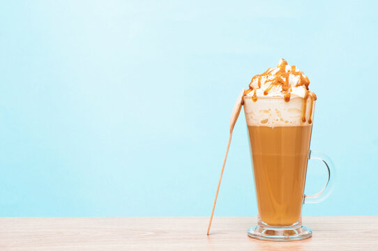 Glass of latte with a spoon on a wooden table colorful blue background. Serving coffee with milk, whipped cream and caramel