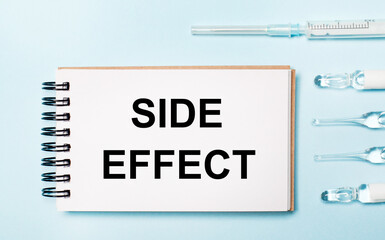 On a blue background ampoule with medicines and a notebook with the text SIDE EFFECT. Medical...