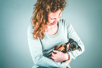 Part of a female, she lovingly holds a tiny sleeping Jack Russel Terrier puppy in her arms. In green vintage, retro colors