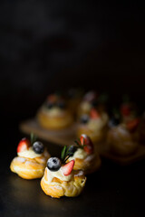 Appetizing profiteroles with cream and fresh berries on a dark background. Image with selective focus