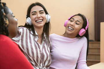 Happy multiracial friends having fun listening music with wireless headphones on house patio - Young people lifestyle concept
