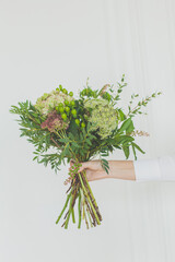 Green flowers and grass  in female hand on white background