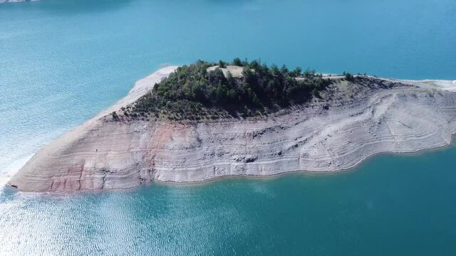 An island in a reservoir in the mountains on the background of turquoise water - drone view