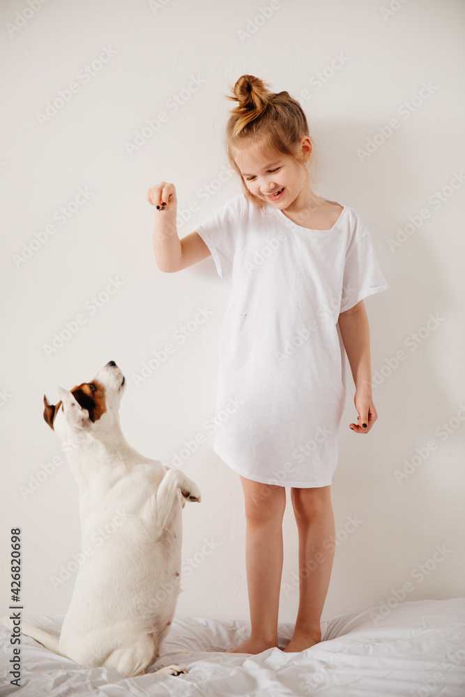 Canvas Prints Beautiful funny kid girl feeds with the palm of hand a dog in white bed. 