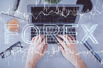 Double exposure of man's hands typing over laptop keyboard and forex chart hologram drawing. Top view. Financial markets concept.