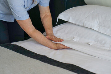 Elderly Maid making bed in hotel room. Housekeeper Making Bed
