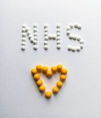 White pills in the form of a yellow heart and the text NHS with medical masks.Medical protective mask isolated on a white background. Healthcare medical coronavirus quarantine, hygiene concept.