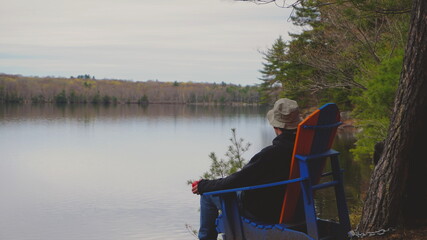 Man sitting in Muskoka chair by the lake. Forest view and lake view.