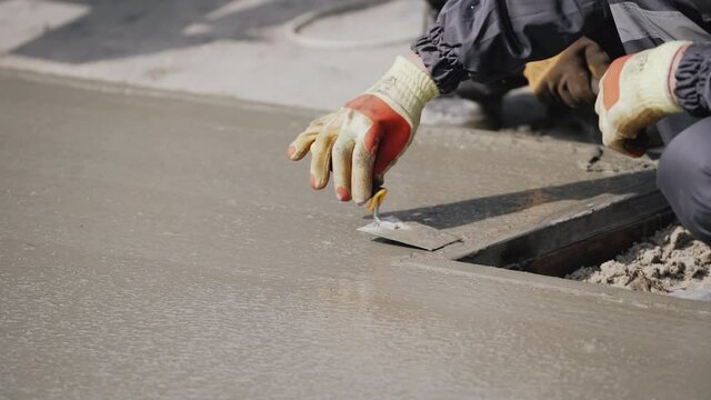 Anonymous Concrete Worker Smoothing Wet Sidewalk. Pouring Concrete. A factory worker uses a shovel to level and smooth wet concrete on a floor