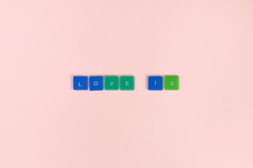 Love is - words made from colored letters on pink background. Top view. Copy space. Selective focus.