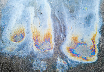 A background of multicolored spots from spilled engine oil on the asphalt. The environmental...