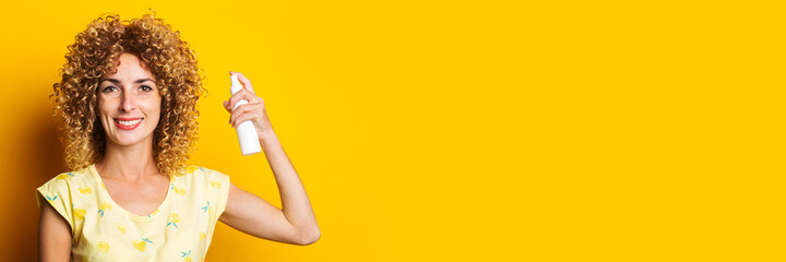smiling young woman moisturizes her hair with a spray on a yellow background. Hair care. Banner
