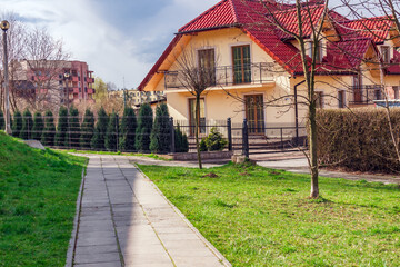 cottage two floors elite house, courtyard with cypress trees sidewalk, in Poland in the spring