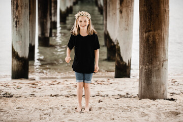 Caucasian girl standing underneath a pier at the beach wearing a flower head band