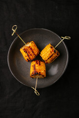 grilled corn on a skewer closeup on dark background. corn with butter and salt top view