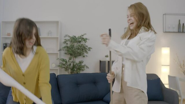 Girls dancing and singing while cleaning the room with vacuum cleaner and broom 