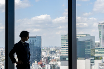 窓から街を眺めるビジネスマン