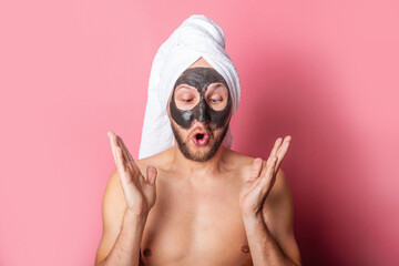 young man looks in surprise at a cosmetic mask on his face on a pink background. Skin care concept.