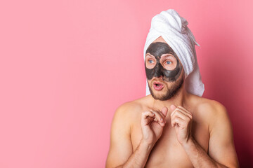 young man applies a moisturizing face mask, looks away in surprise on a pink background