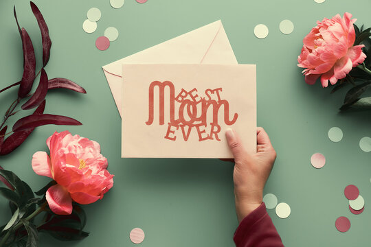 Mother's day greeting card design. Pink peony flowers on faded green background, text Best Mom Ever on paper card with envelope. Trendy casual natural eco friendly flat lay.