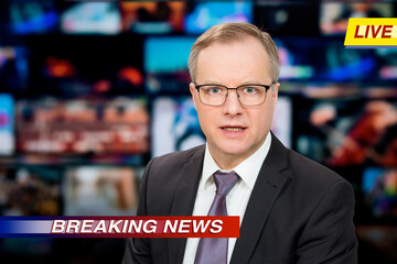 An anchorman reporting live breaking news sitting in Tv studio. Background of multiple screens of broadcast control room. Journalism concept