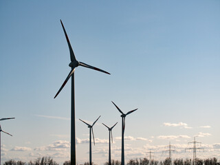 Fototapeta premium Lateral view to some wind turbines on a field in the late afternoon. The sky is clear, only few clouds.