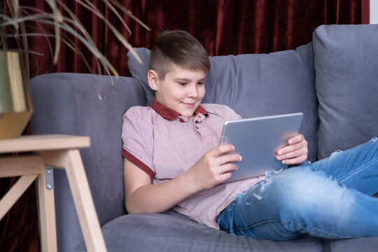 Young handsome teenager boy using tablet sitting on grey sofa at home